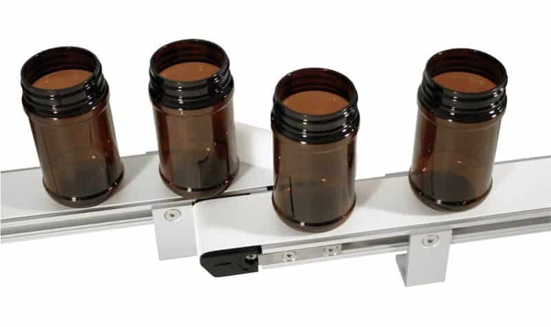 A Dorner 1100 miniature conveyor seamlessly transports empty medicine bottles from one belt to another.